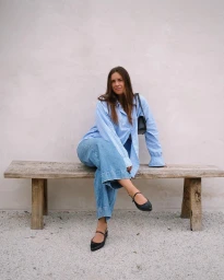 Woman wearing blue striped shirt and wide-leg jeans seated on rustic wooden bench outdoors