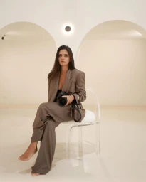 Woman in brown suit sitting on clear acrylic chair holding camera
