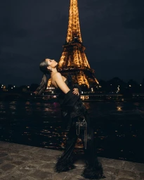 Woman in black feather-trimmed trousers and jacket posing near the Eiffel Tower at night by Karla Paniagua