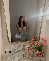 Woman in a green satin dress taking a mirror selfie holding a small sparkly handbag in a bathroom