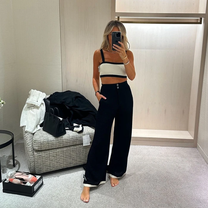 Content creator Roxy Jacenko taking a mirror selfie in a retail dressing room wearing a black and white knit crop top and trousers.