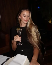Woman with long blonde hair holding a martini glass at a restaurant table, captured by Sophie Jordan.