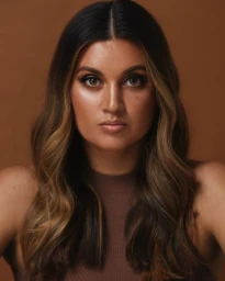 Portrait of Jamila Rizvi with highlighted brown hair wearing a brown top against a warm brown background
