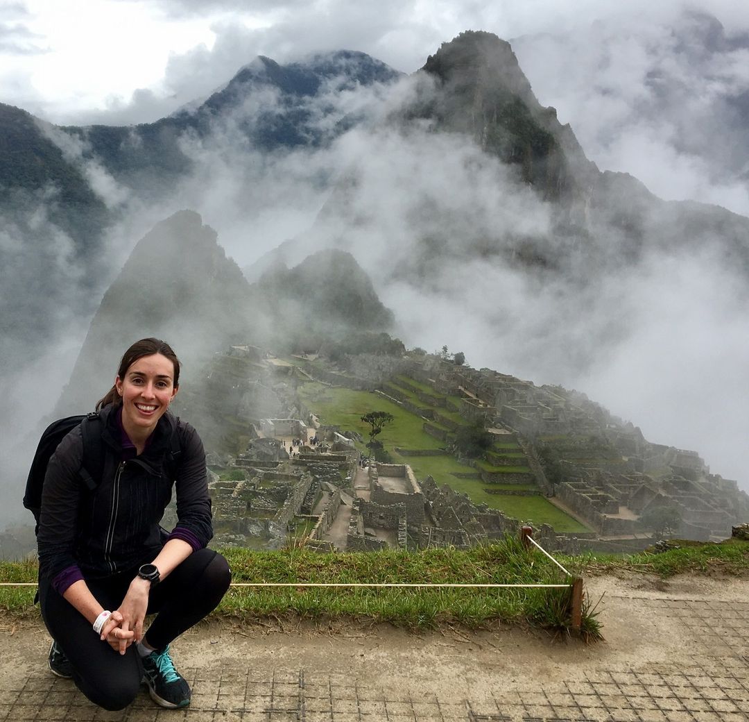 Woman poses near Machu Picchu ruins with mountains and fog backdrop. Tourism in Peru, South America on display in this outdoor shot.
