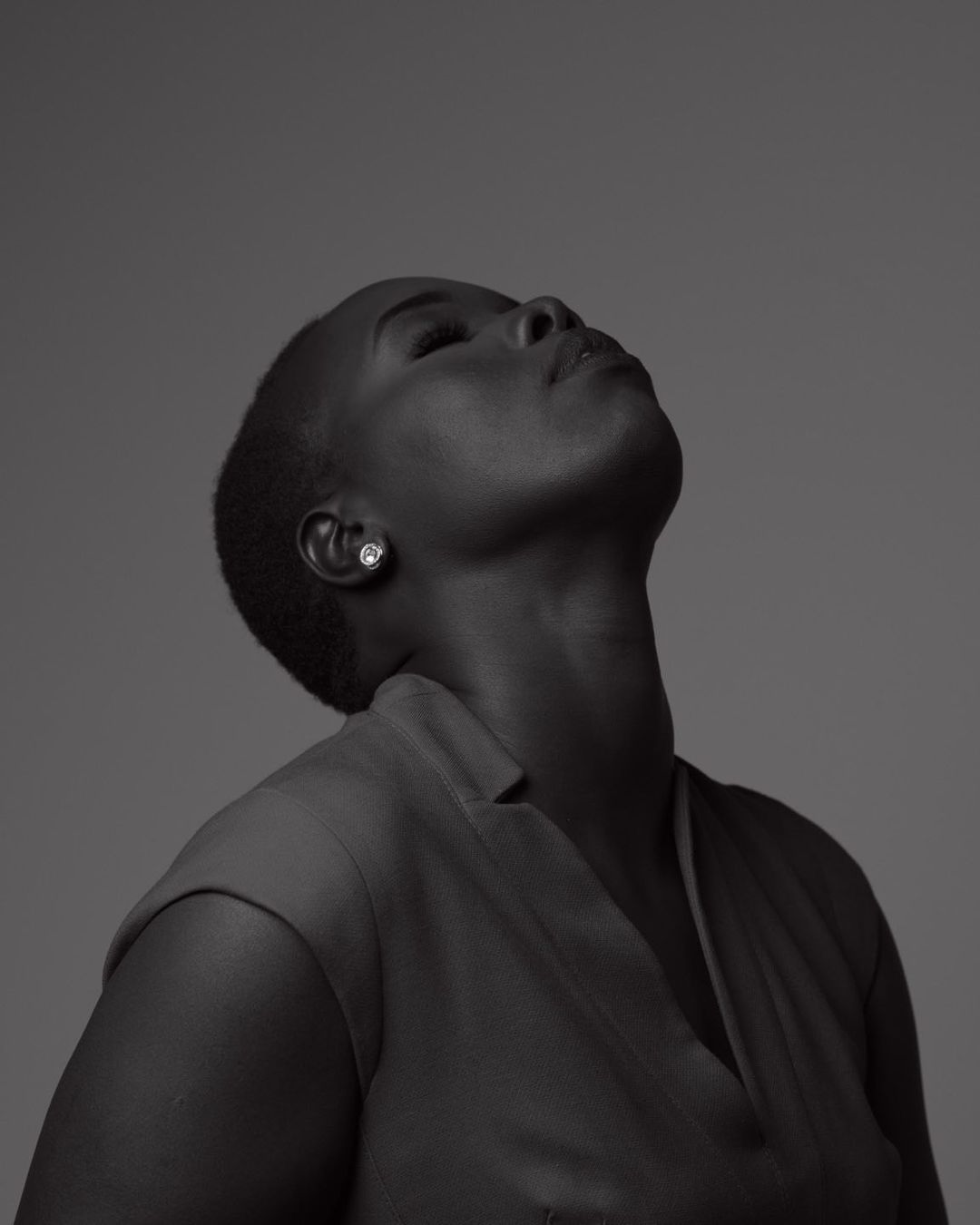Monochrome portrait of an adult woman with short hair, looking upwards with her head tilted back in a photo studio setting.