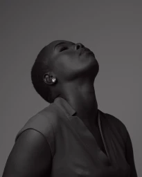 Portrait of Black woman with short hair and earrings tilting her head back in monochrome against a plain grey background