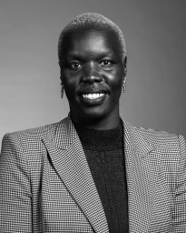 Portrait of Nyadol Nyuon wearing a houndstooth blazer and dark top against a neutral background
