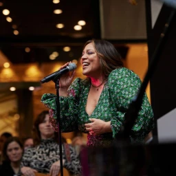 Kate Ceberano singing into a microphone wearing a green floral dress with voluminous sleeves