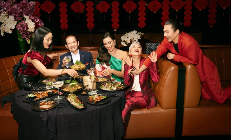Group of six people smiling and dining at a restaurant table featuring various Asian dishes and drinks.