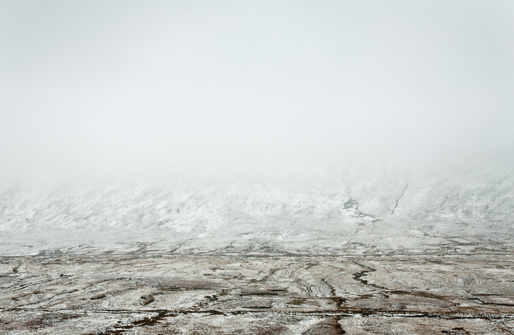 Wide shot of a snowy, mountainous landscape with a cloudy sky, presenting a minimalist and tranquil winter scenery.