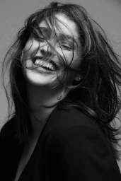 Close up monochrome portrait of smiling woman with long dark hair blowing across face in Melbourne by Tovo