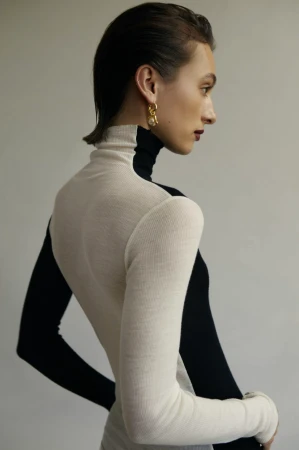 Model with slicked-back hair wearing a black and cream turtleneck sweater against a plain background