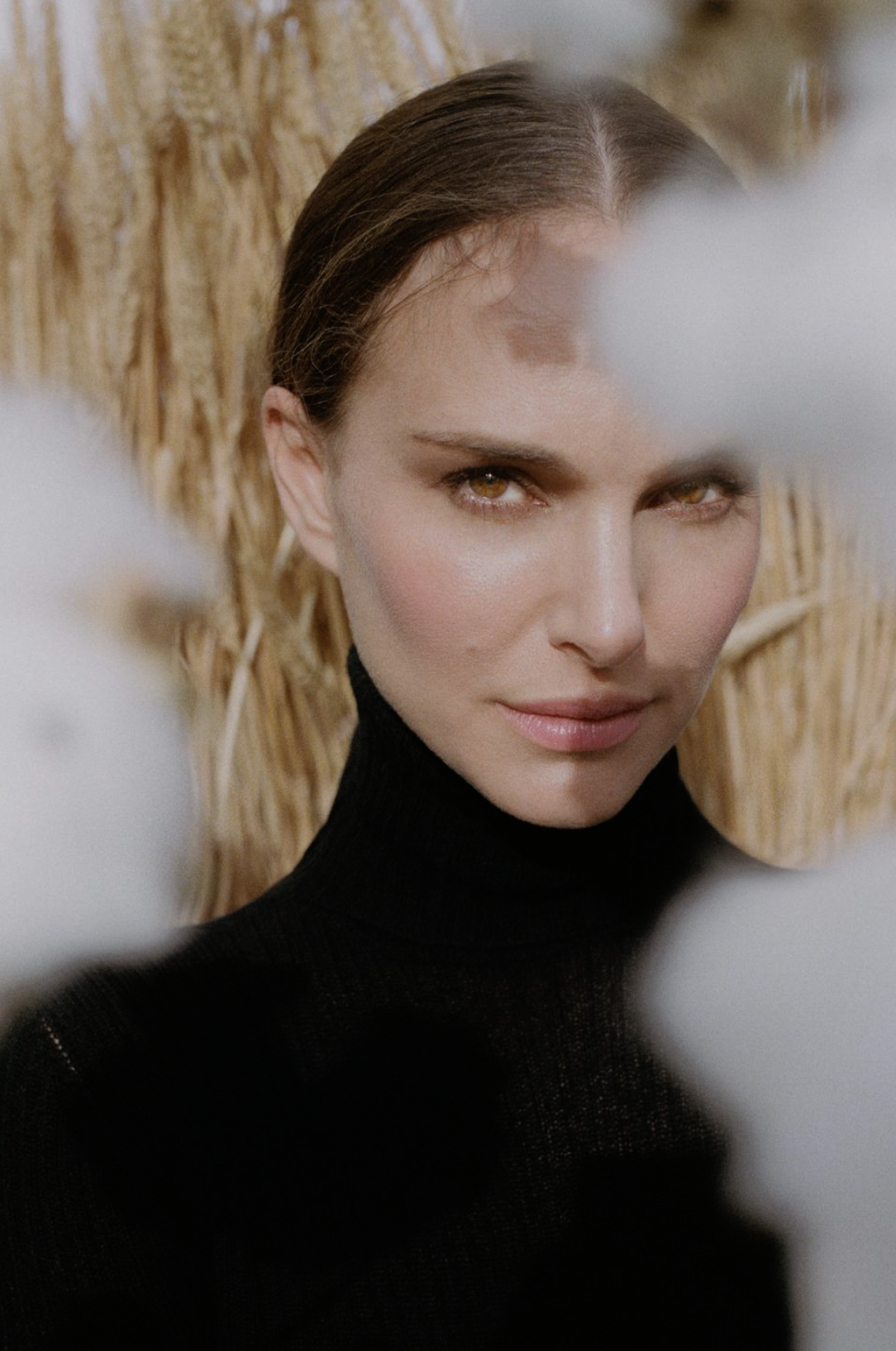 Close-up portrait of a woman with fair skin and brown hair, wearing a black turtleneck sweater, posed in front of a wheat field.