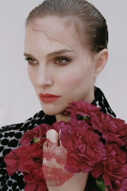 Close-up of a woman with slicked-back hair, holding a bouquet of maroon carnations, wearing a black and white animal print jacket.