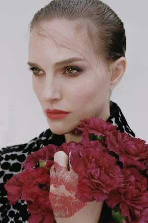 Close-up of a woman with slicked-back hair, holding a bouquet of maroon carnations, wearing a black and white animal print jacket.