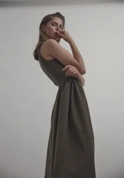 Model in olive green sleeveless dress posing against a plain grey background styled by Sarah Banger