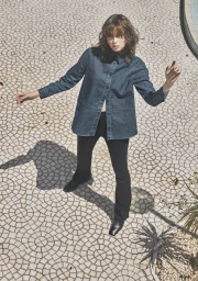 Woman in a dark blue denim button-down shirt and black pants standing on a patterned paved ground