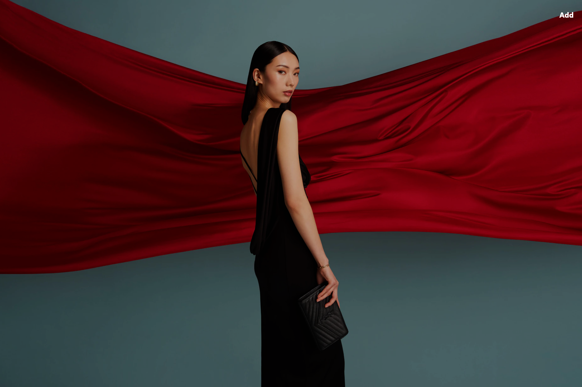 Elegant Asian woman in a black gown poses with a clutch against a red fabric backdrop, captured in a fashion-forward, eye-level shot.