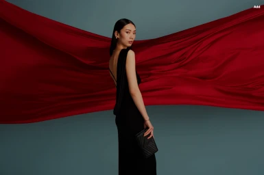 Woman in a black evening gown holding a clutch against a backdrop of flowing red fabric styled by Abby Bennett