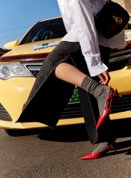 Close-up of a person wearing a white shirt, black skirt, grey socks, and red heels leaning against a yellow car.