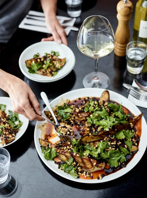 Overhead shot of a table setting with a large salad with greens, potatoes, and sauce, served on white plates alongside a glass of wine.
