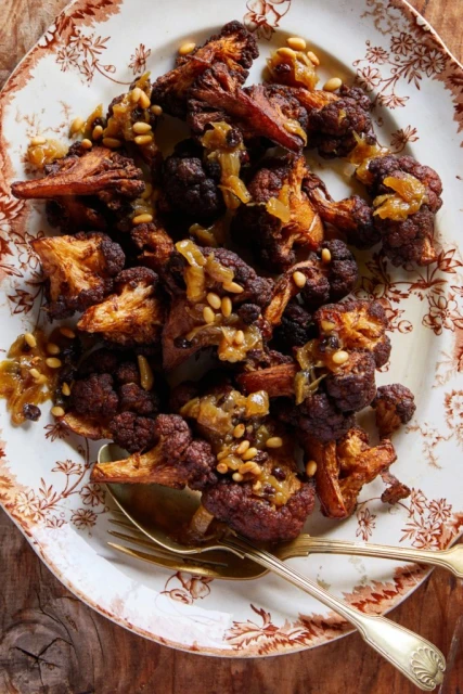 Overhead shot of roasted purple cauliflower with pine nuts on an ornate plate, showcasing a rustic, gourmet presentation for food visuals.