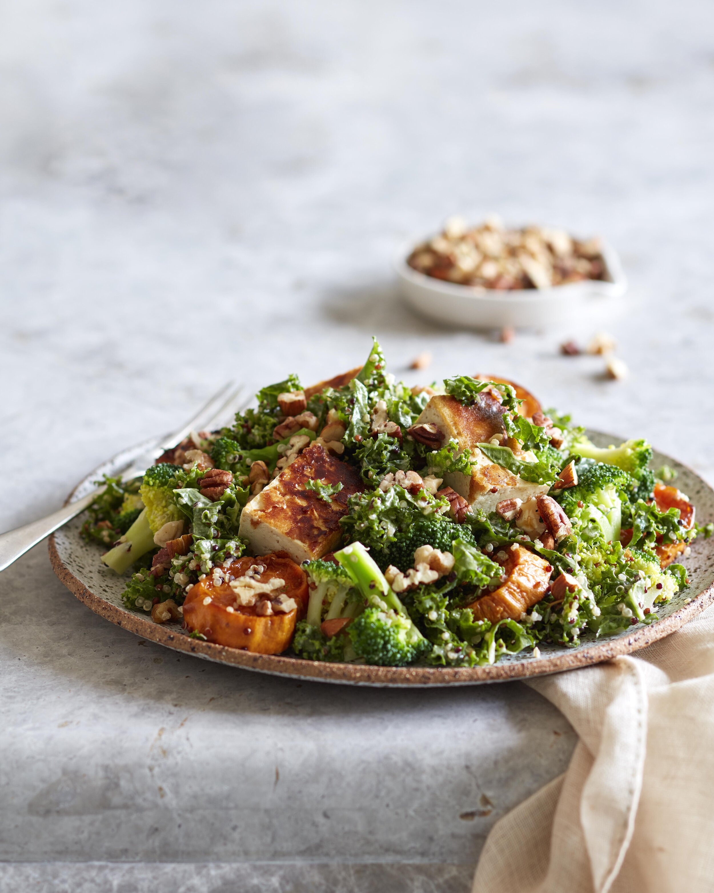Overhead shot of a plate of grilled chicken and vegetable salad with broccoli, kale, squash, and nuts, placed on a marble surface.