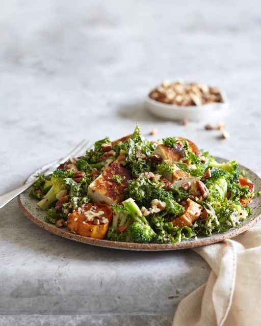 Overhead shot of a plate of grilled chicken and vegetable salad with broccoli, kale, squash, and nuts, placed on a marble surface.