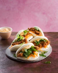 Close-up of fluffy steamed bao buns filled with crispy fried chicken, shredded carrots, and fresh herbs.