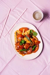 Top-down view of stir-fried tomato and egg on a white plate with pink chopsticks and cup on a pink background.