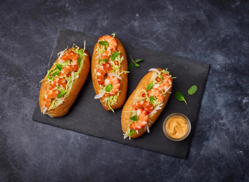 Three shrimp rolls on a black slate plate with dipping sauce and garnished with mint leaves. Food photography for restaurant menu.