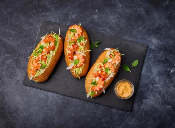 Three shrimp rolls on a black slate plate with dipping sauce and garnished with mint leaves. Food photography for restaurant menu.