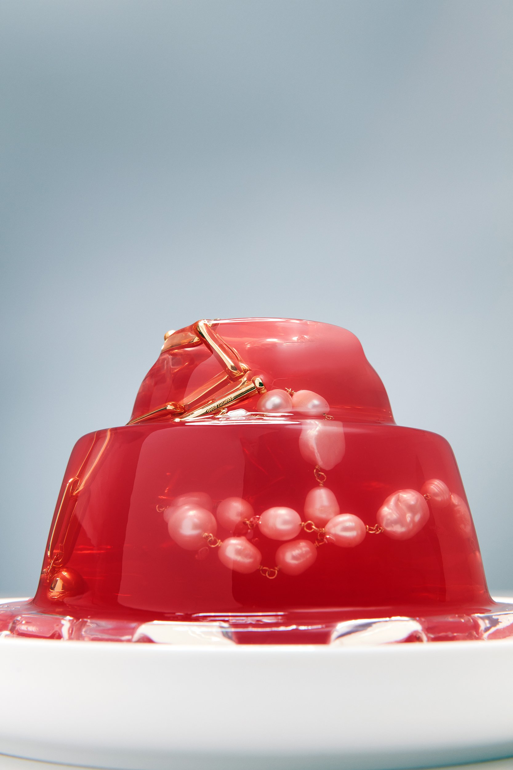 Jello dessert with pearl necklace and gold bracelet on white plate against light blue background, studio shot for food or jewelry.