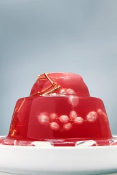 Molded red jelly dessert styled with pink pearl beads and gold jewelry, set against a pale blue and white background.