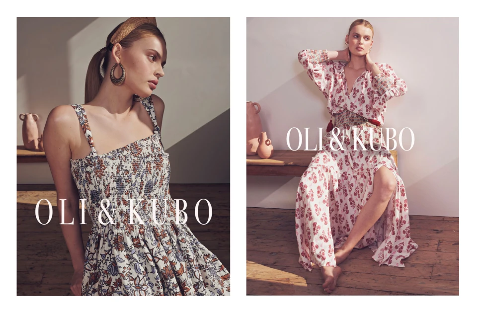 Two young women in floral print dresses by Oli & Kubo pose indoors; one seated with a thigh slit, earrings and a headband.