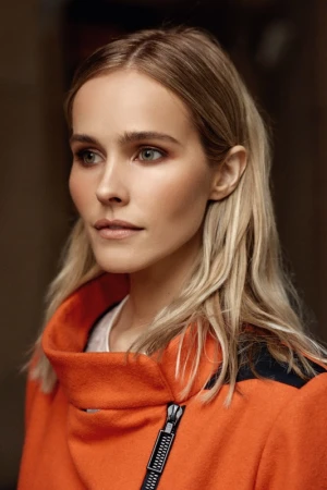 Portrait of a blonde woman wearing an orange zip-up jacket with black shoulder panels.