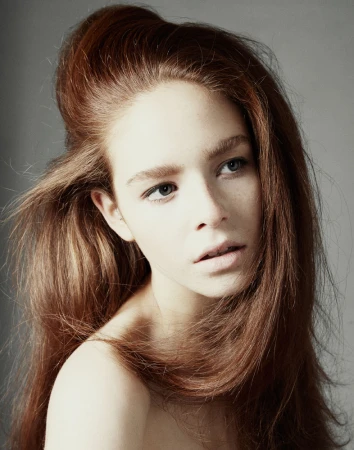 Portrait of a woman with voluminous long brown hair and soft natural makeup against a grey background.