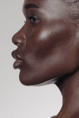 Close-up profile portrait of a black woman with smooth skin and subtle lip gloss against a neutral grey studio background