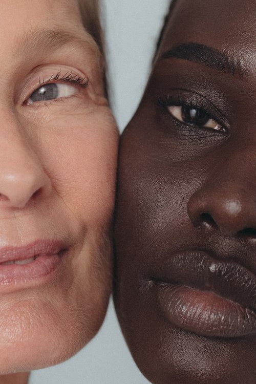 Close-up of two women with different skin tones, one with light skin and blue eyes, the other with dark skin and dark eyes.