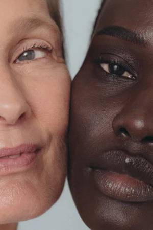 Close-up of two women with different skin tones, one with light skin and blue eyes, the other with dark skin and dark eyes.