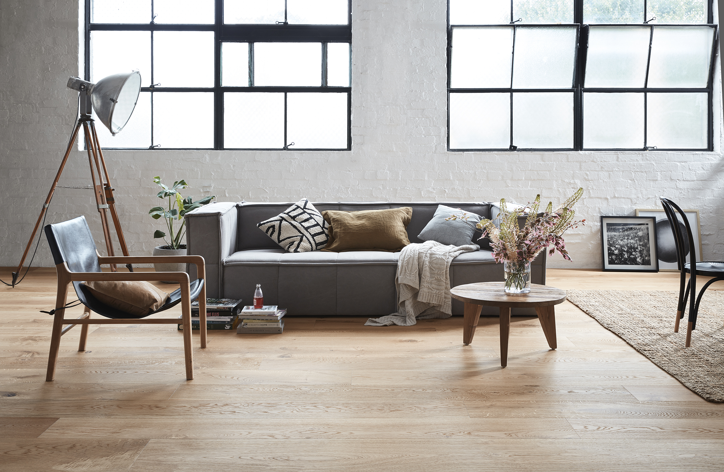Living room interior with gray sofa, wooden chair, coffee table, and large windows letting in natural light. Home interior with furniture.