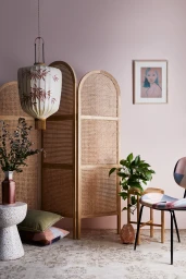 Interior styling by Rachel Vigor featuring a rattan folding screen, patterned chair, and hanging lantern against a soft pink wall