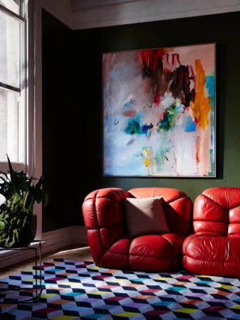 Interior design featuring a red leather modular sofa, a colorful geometric rug, a modern art piece, and a green potted plant.