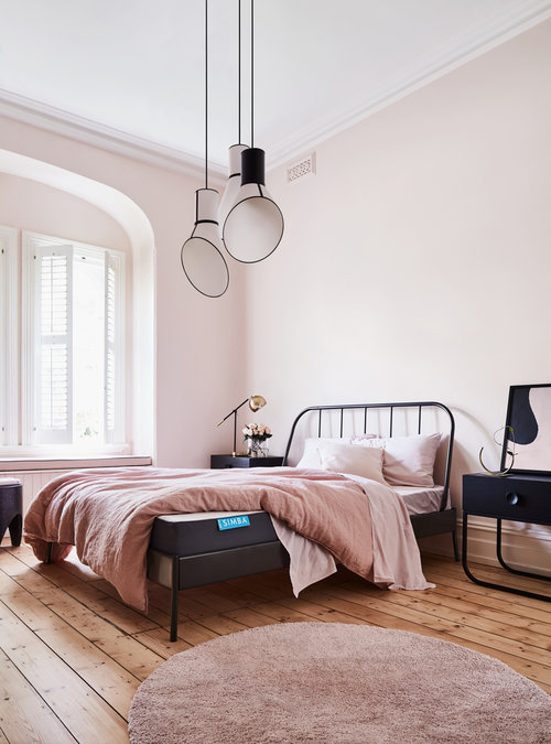 Bedroom interior featuring a wrought-iron bed with pink bedding, wooden flooring, and three modern pendant lights hanging above.