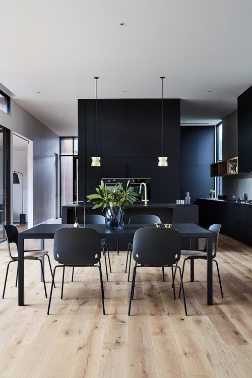 Modern dining room interior with black table and chairs, minimalist decor, wooden floors, and contemporary pendant lights in a home setting.