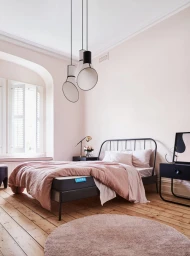 Modern bedroom interior styled by Heather Nette King featuring a black metal bed, pink linens, and contemporary pendant lights.