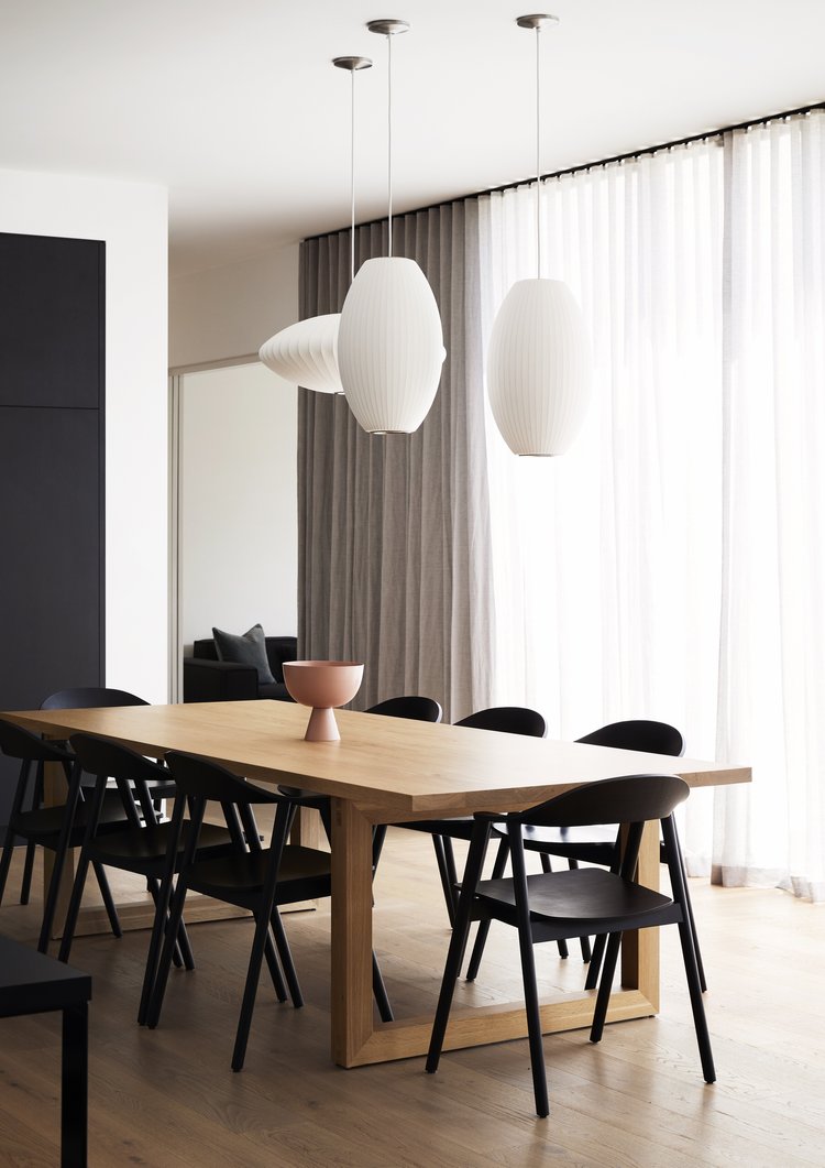 Interior view of a dining room featuring a light wood table with black chairs, a modern bowl, and stylish pendant lights above.