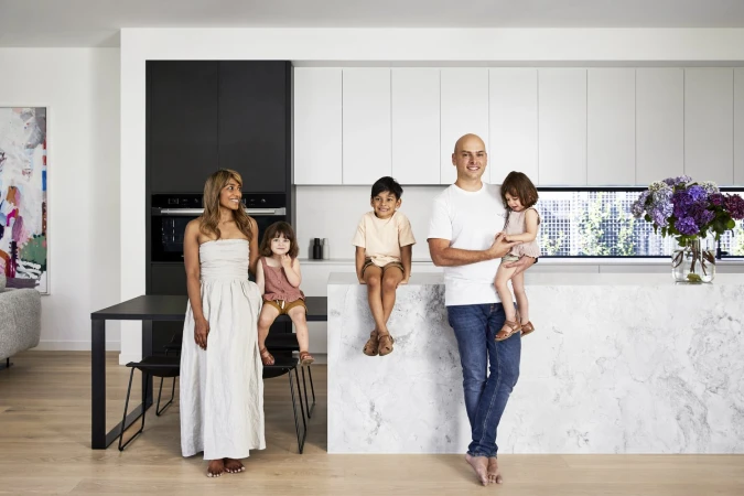Family of five in modern kitchen with white marble island, black and white cabinets, and light wood floors, creating an inviting space.