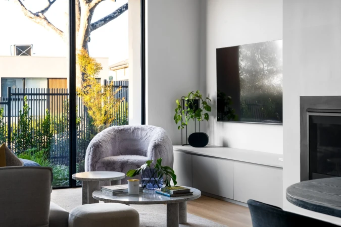 Living room interior featuring a plush gray armchair, marble coffee tables, and a view to the exterior garden with black metal fence.