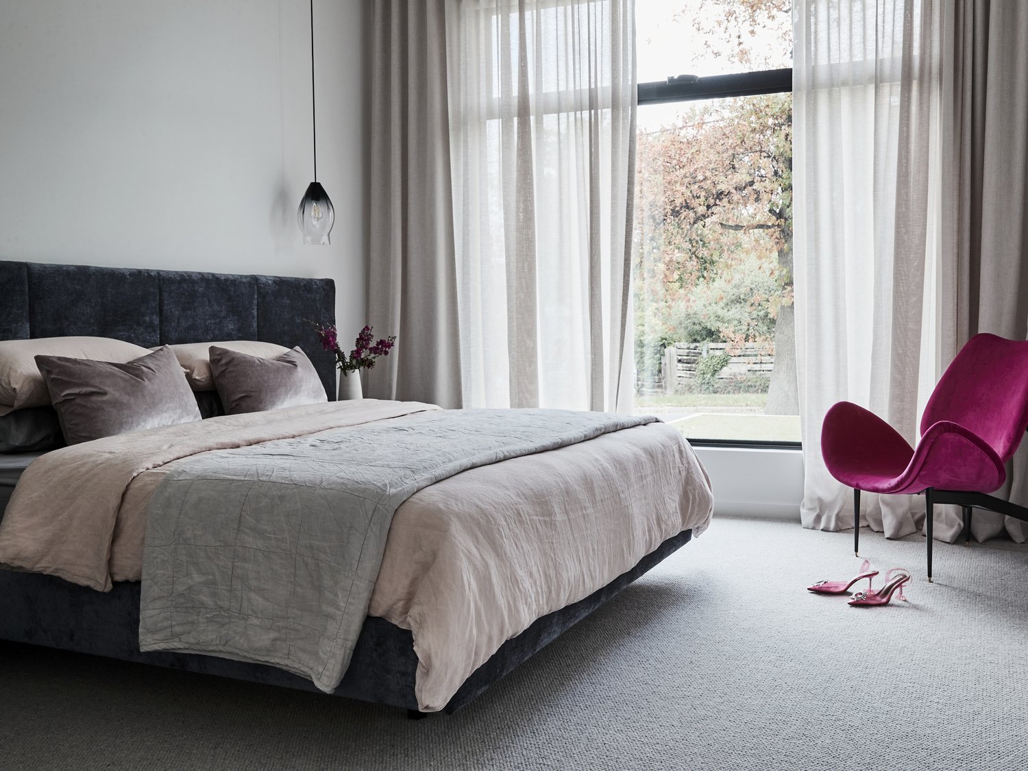 Interior of a bedroom with a large bed, pink chair, and shoes. Neutral colors and soft lighting create a calming atmosphere.